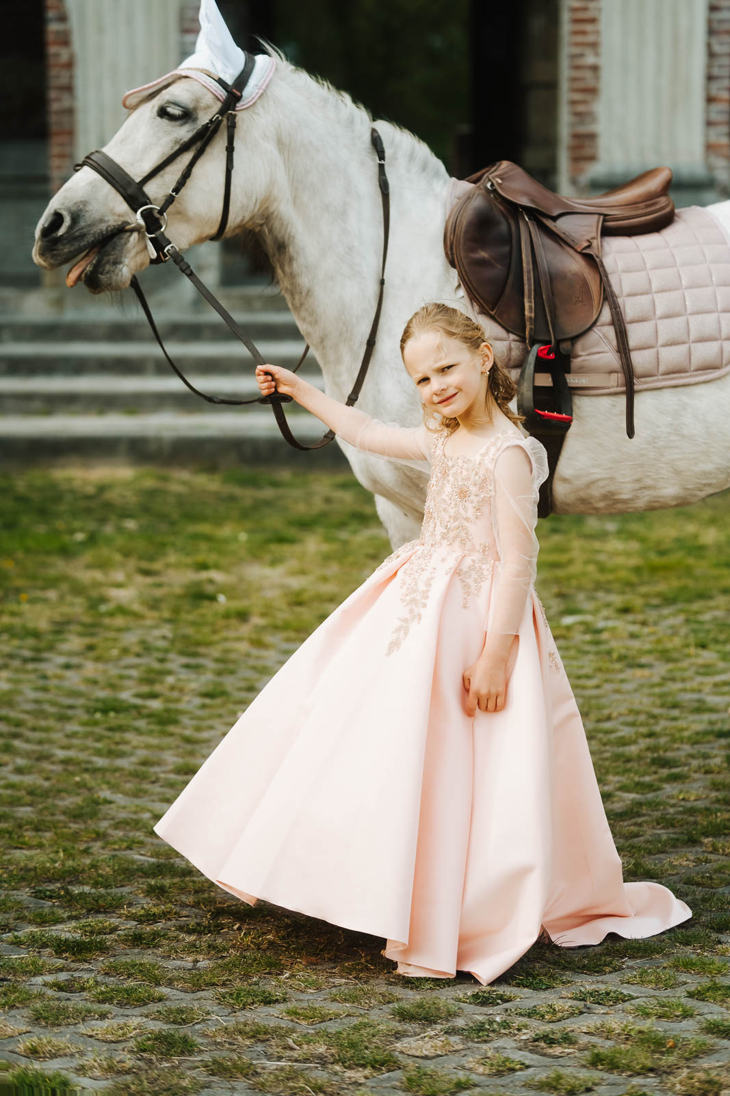 Meisje in een roze communiejurk leidt een wit paard aan de teugel voor het Kasteel van Mesen in Lede