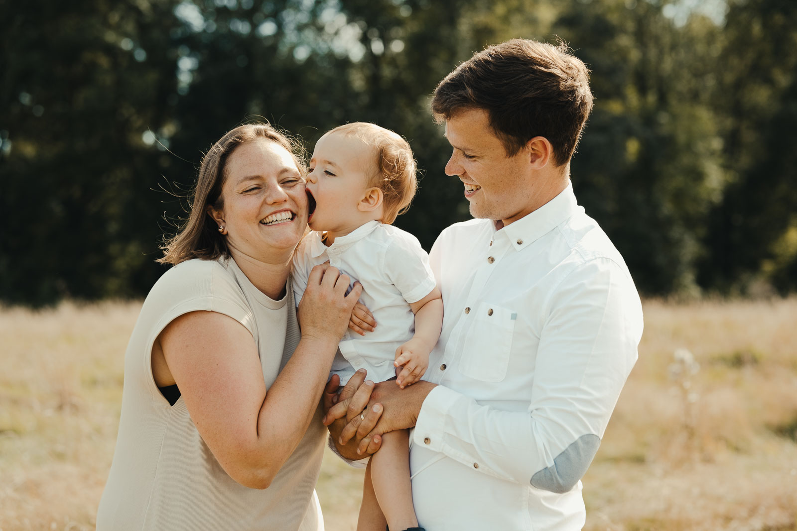 Ouders in het wit knuffelen hun peuter tijdens een gezinsshoot in het gouden uur in Wichelen