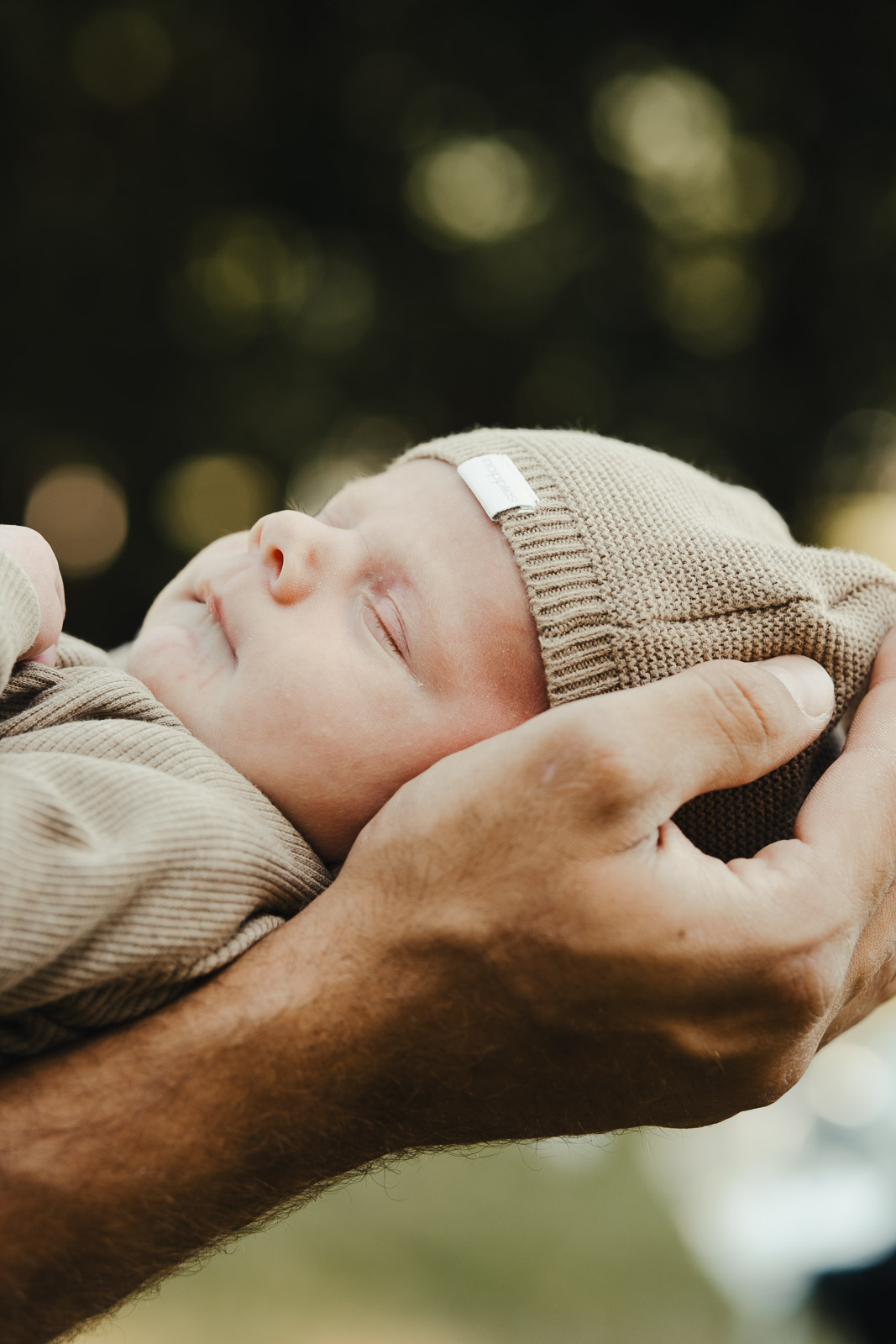 Pasgeboren baby in beige wikkeldoek in de handen van papa, newbornfotografie in Wichelen