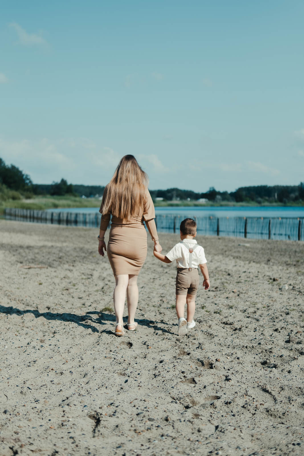 Zwangere mama wandelt hand in hand met haar zoontje over het strand aan het water